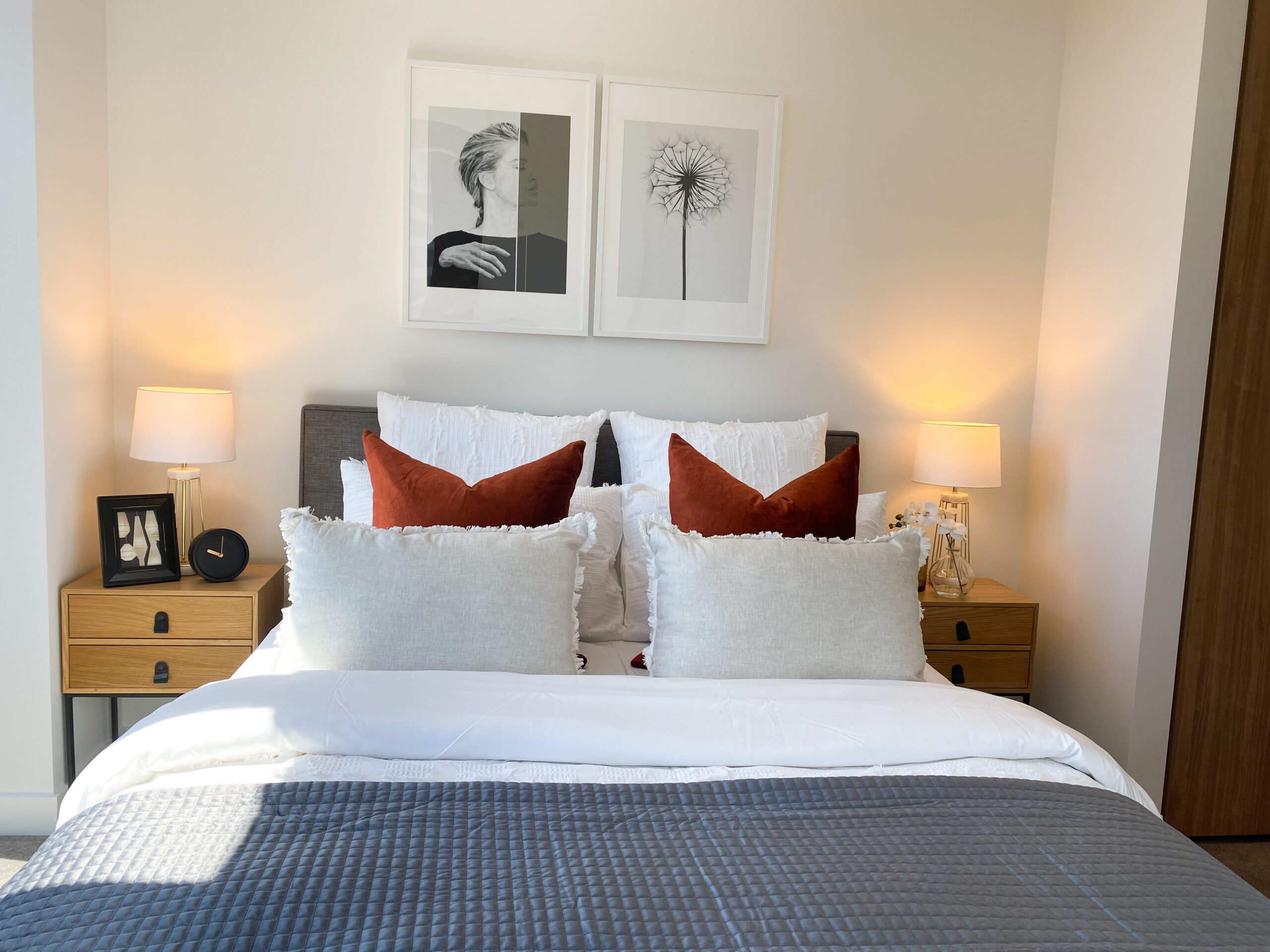 Modern bedroom with decorative burnt orange cushions. Two pieces of art above the bed. Chopped cushions.