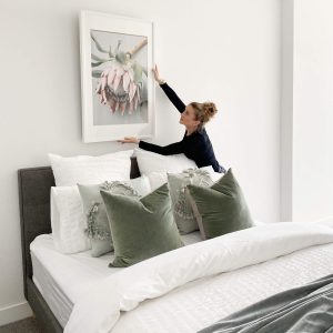 Hanging art over bed white room with sage cushions